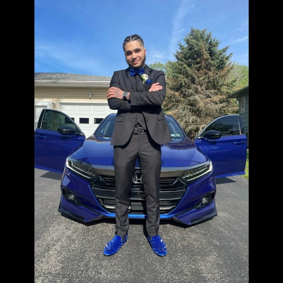 Client in black suit with blue crystal loafers and bow tie posing with blue car